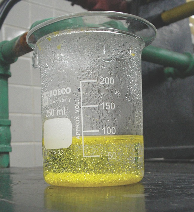 A photograph is shown of a yellow green opaque substance swirled through a clear, colorless liquid in a test tube.
