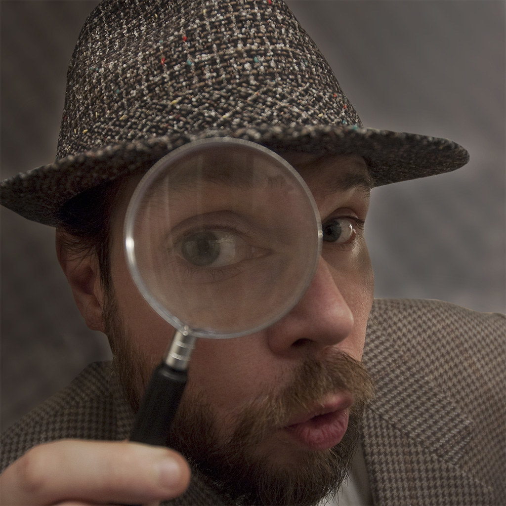 “The Detective” by paurian is licensed under CC BY 2.0 Photo showing person looking at camera through a magnifying glass