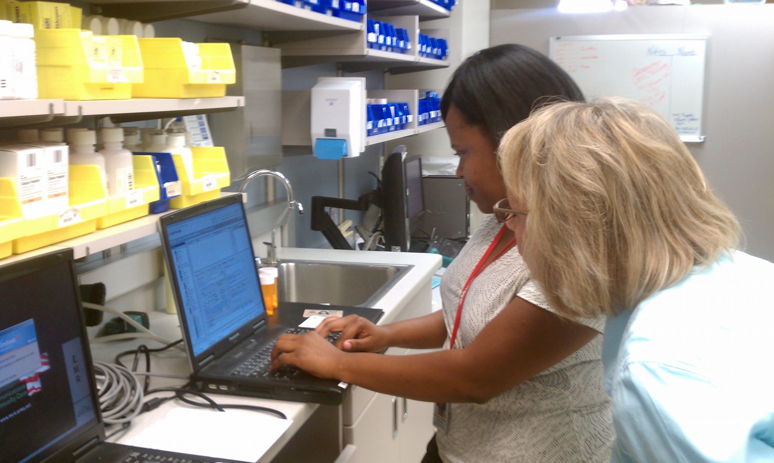 "Winn_Army_Community_Hospital_Pharmacy_Stays_Online_During_Power_Outage.jpg" by Flickr user MC4 Army is licensed under CC BY 2.0 Image showing two nurses in a pharmacy, entering information into electronic health record on a laptop
