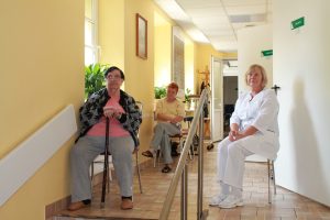 “35528913166_1a61470157_h.jpg” by Senior Guidance is licensed under CC BY 2.0 Image showing elderly three older women sitting in a hallway, facing camera