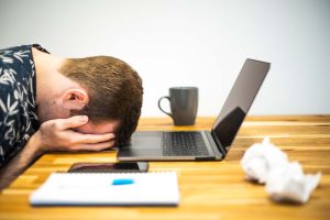 “Burnout_At_Work_-_Occupational_Burnout.jpg” by Microbiz Mag is licensed under CC BY 2.0 Image of man with head in hands, facedown on a desk. Laptop and office supplies around him.
