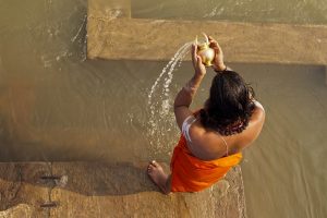 “hindu-1588337_960_720.jpg” by gauravaroraji0 is licensed under CC Image showing a persona pouring water into a larger body of water, as in Worship with Water
