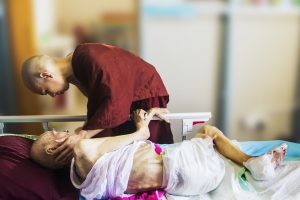 “hospice-1794912_960_720.jpg” by truthseeker08 is licensed under CC0 Image showing a monk leaning over a hospice patient and touching their face