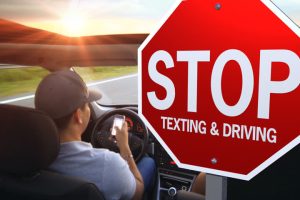 “texting-while-driving/man-texting-while-driving-md.jpg” by unknown at QuoteInspector.com is licensed under CC BY-ND 4.0. Photo showing car driver looking at cell phone with large stop texting and driving sign beside them
