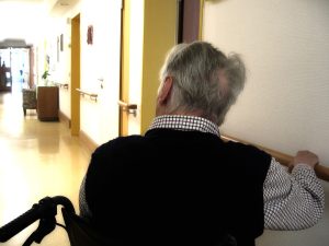 “old-63622_960_720.jpg” by geralt is licensed under CC0 Image showing elderly man in wheelchair looking down a hallway