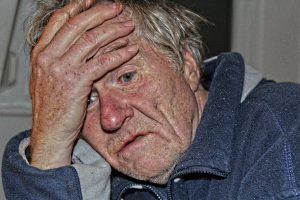 “old-peoples-home-524234_960_720.jpg” by mikegi is licensed under CC0 Image of older man with their hand on their forehead.