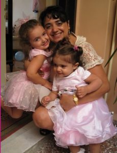 Image of a woman kneeling and holding two toddlers, ages approximately 2 and 3 years