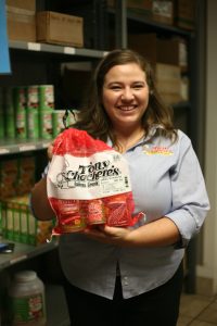 Image of a female employee holding up a gift bag of Tony Chachere's products in front of shelves of inventor at the Tony Chacere's seasonings headquarters in Opelousas, Louisiana.