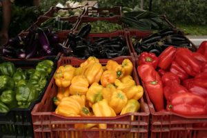 Image of green, yellow, red, and purple peppers in crates at a farmers market
