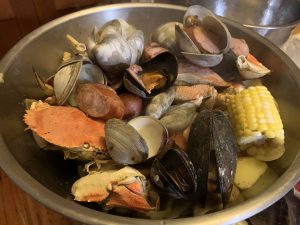 Image of a seafood boil with crabs, sausage, oysters, corn potatoes, and corn in a metal bowl