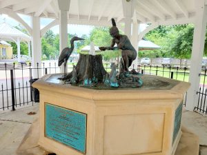 Image of a bronze sculpture of a Native American woman drinking from a spring issuing from a tree stump with an egret looking on.