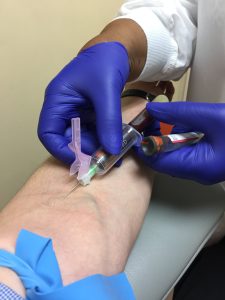 Photograph of a healthcare provider drawing blood from a patient's arm.