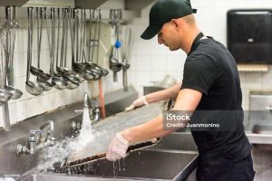 A man washing a pan in a three compartment sink