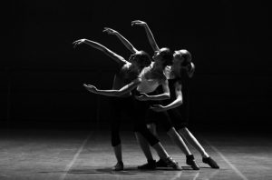 Black and white image of three dancers in a row with righ tarm extended.