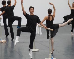 A group of dancers grasping a barre and perfoming a dance move.