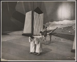 Stage with two costumed performers leaning forward and two ballet dancers dancung