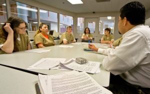A group of people in beige uniforms seated around a table with documents and a small box, engaged in a discussion.