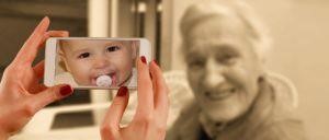 a mother with cell phone camera showing photo of her baby against the backdrop of her smiling mother in a black and white photo
