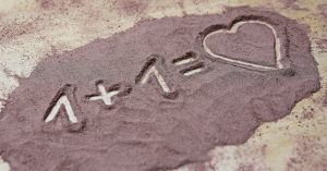 on a sandy beach, someone has drawn the math formula ' one plus one equals a heart symbol'