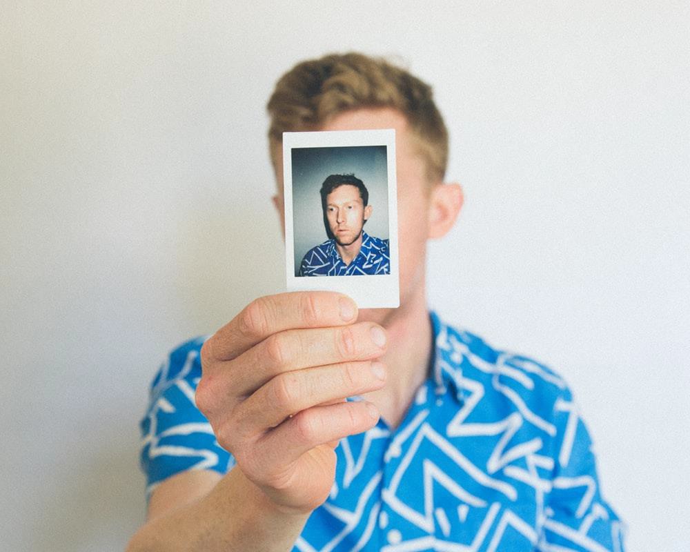 A man holding a polaroid photo in front of his face.