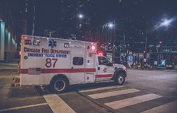Ambulance with flashing lights driving through an intersection.