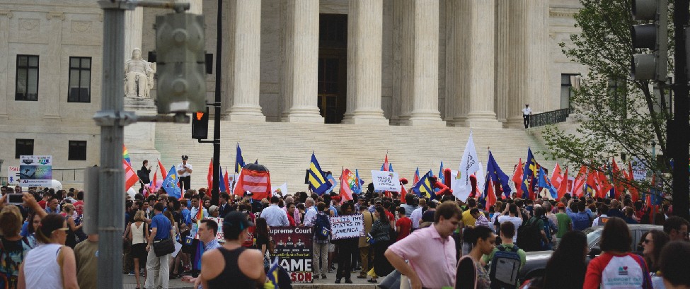 Group of people at the steps of the Supreme Court building. Many people are holding flags marked with the symbol of an equals sign.