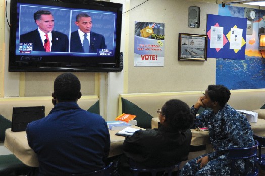 Three people watching a television. On the television screen are Mitt Romney and Barack Obama.
