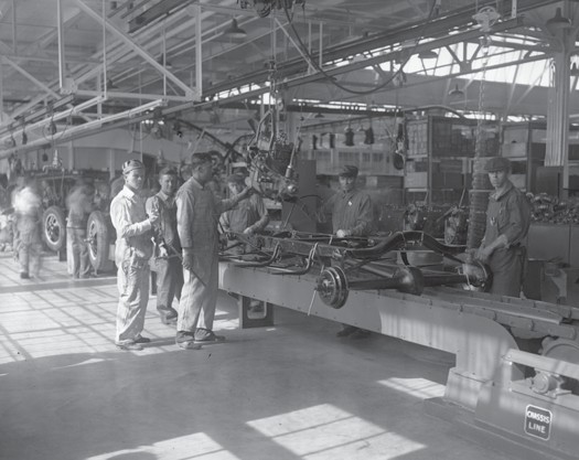 People standing in an automotive plant next to some machinery.