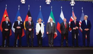 Ministers of foreign affairs and other officials standing on a stage, each in front of the flag of their country.
