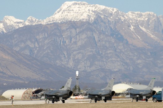 Several grounded fighter jets, with a mountain range in the background.