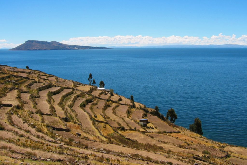 Ancient terraces of land and shrubbery at the edge of a large blue lake and island in the distance