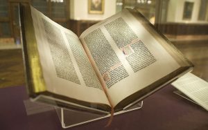 The Gutenberg Bible opened with gold-edged pages, dark block text, and two hand-colored initial letters