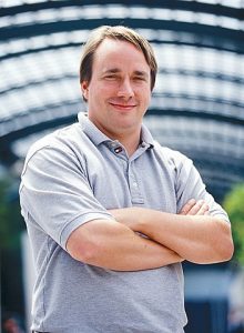 Colored photograph of Linus Torvalds in grey short sleeved shirt with arms crossed over chest