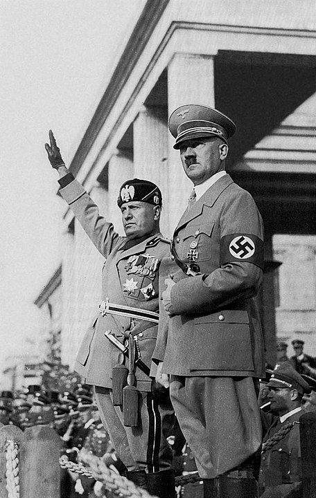 Benito Mussolino (left) with gloved hand raised in Roman salute standing next to Adolf Hitler in Nazi uniform