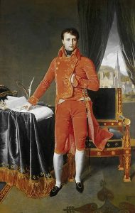 Napoleon stands next to a cloth-covered table with his hand on a document