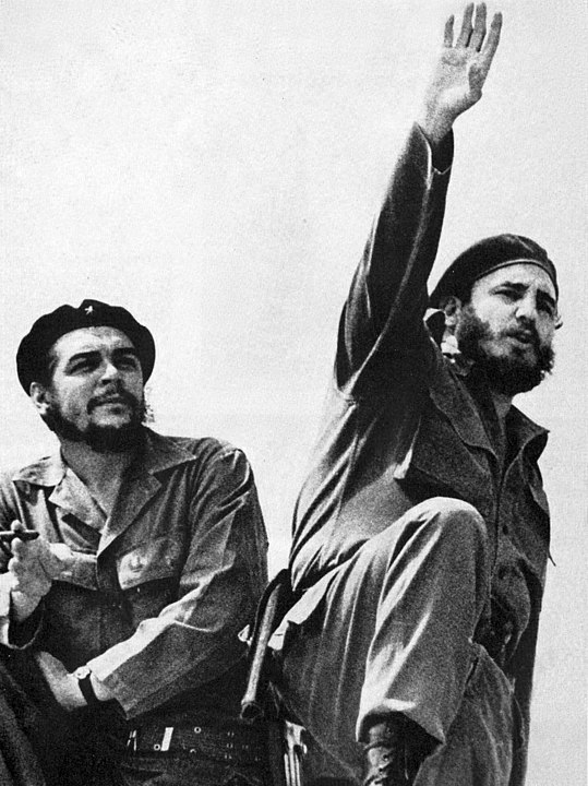 Che Guevara holding cigar standing next to Fidel Castro with arm outstretched