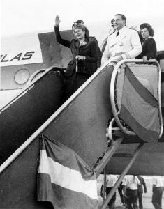 Juan Perón in white suit standing next to his wife, Evita, at the door of an airplane as she waves
