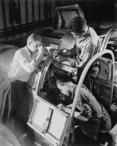 Three African-American workers work to complete the pilot's compartment of an aircraft