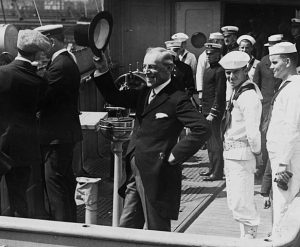 President Woodrow Wilson (center) waves his top hat from the deck of USS George Washington on his return voyage from the Versailles Peace Conference with naval personnel to his left