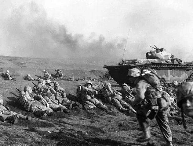 A battalion of U.S. Marines positioned on the ground and with a tank waiting to move inland on Iwo Jima