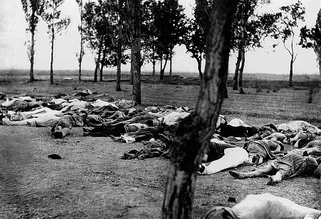 Scene of the Armenian genocide showing large group of people in various states of undress lying dead on the ground in a grove of trees