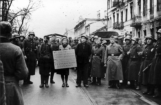 Masha Bruskina walking down street surrounded by German troops before her execution with a sign that reads "We are the partisans who shot German troops"