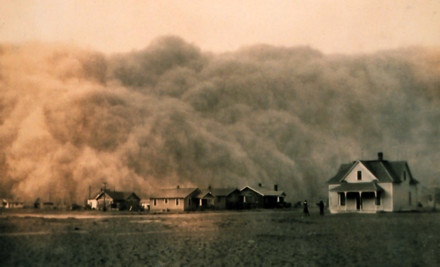 A large cloud of dust fills the sky as a dust storm approaches a group of homes