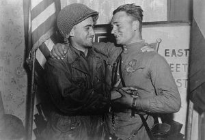 2nd Lt. William Robertson (U.S. Army) and Lt. Alexander Silvashko (Red Army) stand facing one another with hands clasped and arms around each other’s shoulders