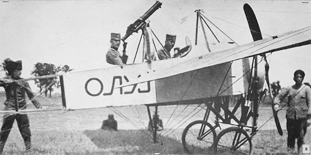 Two men in first Serbian armed airplane powered by propeller with forward-facing gun at rear of plane