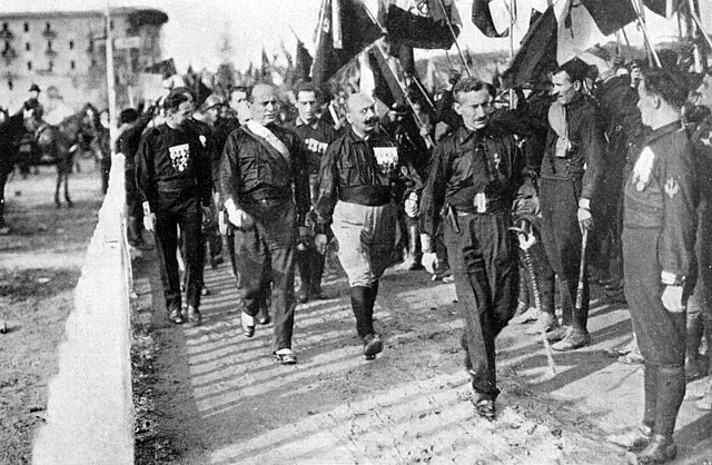 Group of men, known as Blackshirts, march with Benito Mussolini in Rome, many holding flags