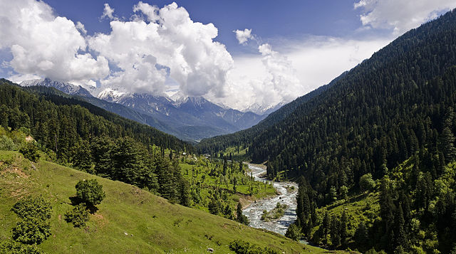 A river runs between a mountain valley (Pahalgam Valley) with clouds and mountains in the distance
