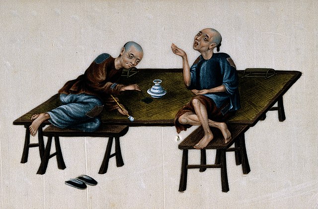 Two Chinese men laying on a table smoking opium