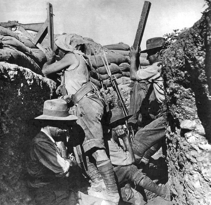 Three Australian soldiers in a trench firing a periscope rifle from inside the trench at Gallipoli