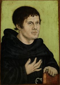 Martin Luther dressed in dark monk's robe with belt and silver buckle; his left hand on top of a brown book and right hand held open at chest